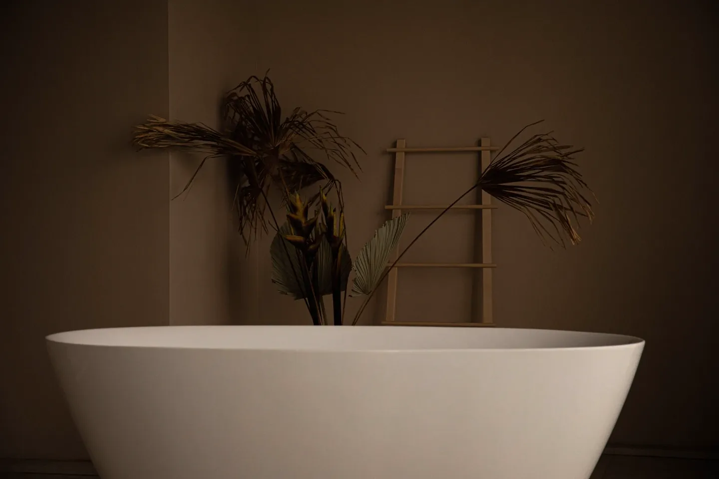 A quiet bathroom with warm plaster walls, a bath, foliage, and a wooden ladder